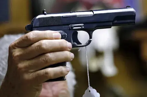 A sales clerk holds a pistol during an auction in Rochester, Wash., on Oct. 20, 2017. A study published in Annals of Internal Medicine on Monday, April 4, 2022, suggests people who live with handgun owners are murdered at more than twice the rate of people who live in homes without such firearms. (AP Photo/Elaine Thompson, File)