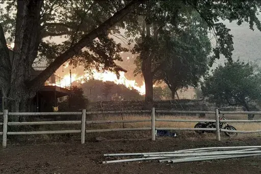 In this photo provided by Alison Oszman, a fast-moving wildfire near the Orego-Idaho border moves toward a home on Rye Valley Lane in Huntington, Ore., in the afternoon o fWednesday, July 24, 2024. (Alison Oszman via AP Photo)