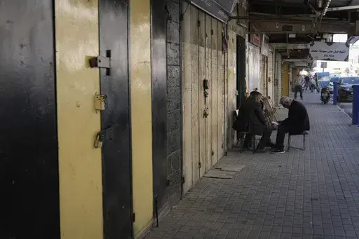 Palestinians sit in front of closed shops during a general strike called as Palestinian security forces mount a major raid against militants in the Jenin refugee camp in the Israeli-occupied West Bank, Monday, Dec. 23, 2024. (AP Photo/Majdi Mohammed)