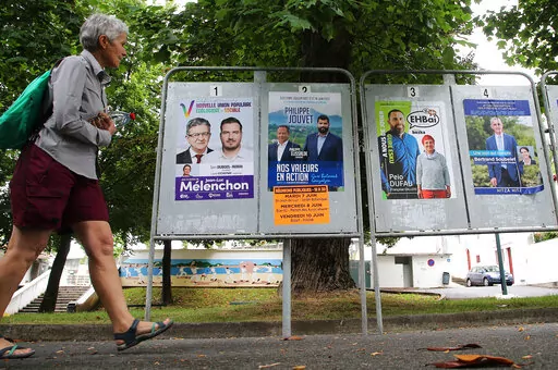 A woman walks past electoral posters of the upcoming parliamentary elections in Saint Jean de Luz, southwestern France, Wednesday June 8, 2022. The legislative elections will take place on June 12 and 19, 2022. (AP Photo/Bob Edme)