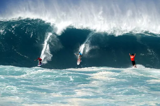 Kai Lenny, left, and Aaron Gold, center, are cheered on by Jake Maki, right, in Hawaii's Waimea Bay on Oahu’s North Shore during the The Eddie Aikau Big Wave Invitational surfing contest Sunday, Jan. 22, 2023. (Jamm Aquino/Honolulu Star-Advertiser via AP)