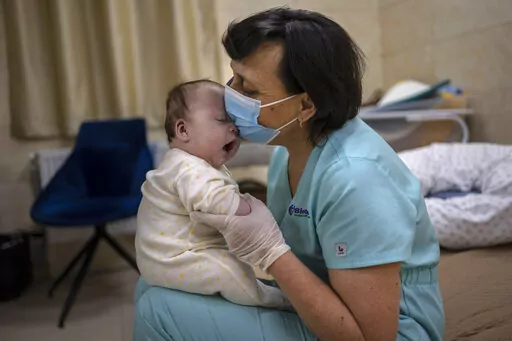 Nanny Svitlana Stetsiuk plays with one of the babies in the nursery in Kyiv, Ukraine, Saturday, March 19, 2022. Nineteen babies are cared for that were born to surrogate mothers. The babies' biological parents are outside the country due to the war against Russia. (AP Photo/Rodrigo Abd)