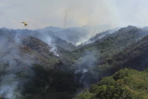 This photo provided by the Hawaii Department of Land and Natural Resources shows an Army helicopter carrying water to douse a wildfire burning east of Mililani, Hawaii, on Thursday, Nov. 2, 2023. A wildfire that has burned forestlands in a remote mountainous area of Central Oahu has moved eastward and away from population centers as firefighters continued to battle the blaze. (Dan Dennison/Hawaii Department of Land and Natural Resources via AP)