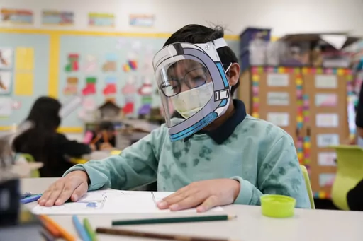 A student wears a mask and face shield in a 4th grade class amid the COVID-19 pandemic at Washington Elementary School on Jan. 12, 2022, in Lynwood, Calif. Four years after the COVID-19 pandemic closed schools and upended child care, the CDC says parents can start treating the virus like other respiratory illnesses. (AP Photo/Marcio Jose Sanchez, File)