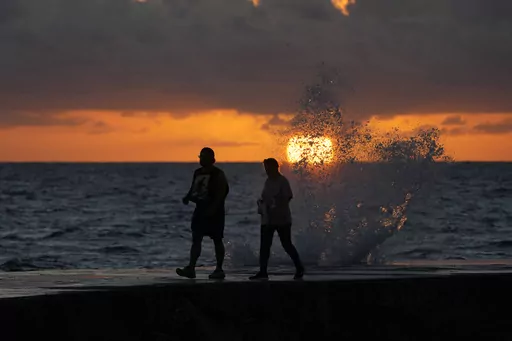 The sun rises above the Atlantic Ocean as waves crash near beach goers walking along a jetty, Dec. 7, 2022, in Bal Harbour, Fla. The world's oceans have suddenly spiked much hotter and well above record levels, with scientists trying to figure out what it means and whether it forecasts a surge in atmospheric warming. (AP Photo/Wilfredo Lee, File)