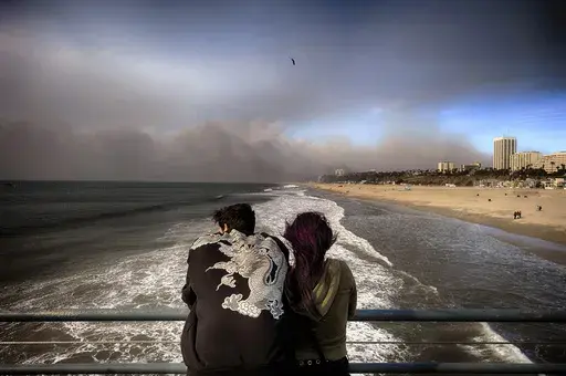 Visitors to the Santa Monica pier look out at smoke from a wildfire in the Pacific Palisades blows over the beach in Santa Monica, Calif., on Wednesday, Jan. 8, 2025. (AP Photo/Richard Vogel)