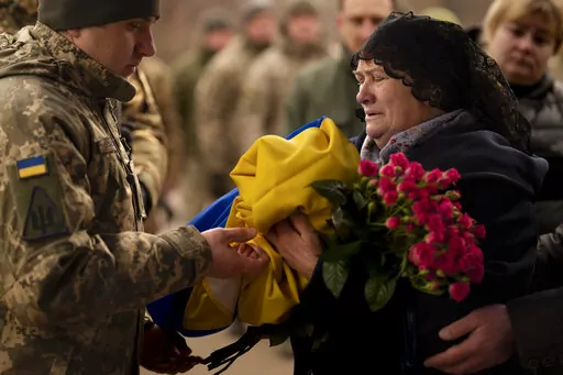 Tetiana Hurieieva, the mother of Volodymyr Hurieiev, a Ukrainian soldier killed in the Bakhmut area, receives the flag that draped his coffin, during the funeral in Boryspil, Ukraine, Saturday, March 4, 2023. Pressure from Russian forces mounted Saturday on Ukrainians hunkered down in Bakhmut, as residents attempted to flee with help from troops who Western analysts say may be preparing to withdraw from the key eastern stronghold. (AP Photo/Vadim Ghirda)