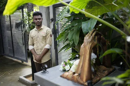 Jayarasa Abilash, known as Baby 81 after he was swept away by the 2004 Indian ocean tsunami, stands in front of a monument built in memory of tsunami victims outside his residence in Kurukkalmadam, Sri Lanka, Tuesday, Dec. 17, 2024. (AP Photo/Eranga Jayawardena)